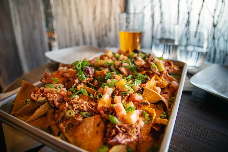 A sheet-pan of loaded pulled-pork nachos with tomato, jalapeño and spring onion served with a cold beer in the Tsaina Lodge dining room